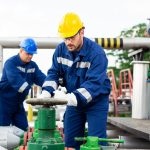 Two petrochemical workers inspecting pressure valves on a fuel tank